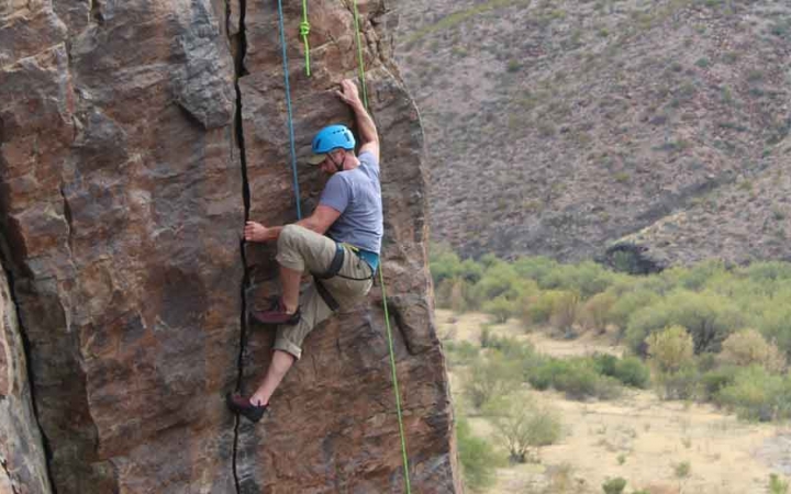 a gap year student rock climbs above a desert landscape in texas